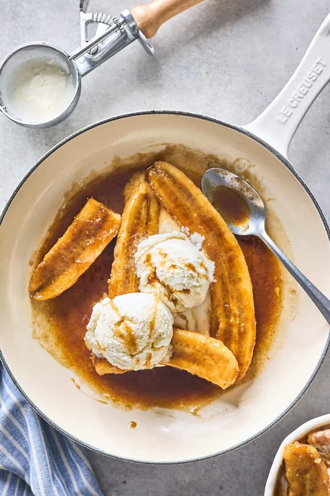 Bananas foster in a skillet with vanilla ice cream served on top against a gray background