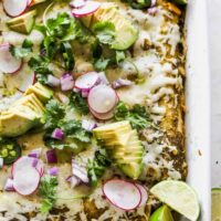 A close up of blackened chicken enchiladas with melty cheese, avocado and cilantro on top