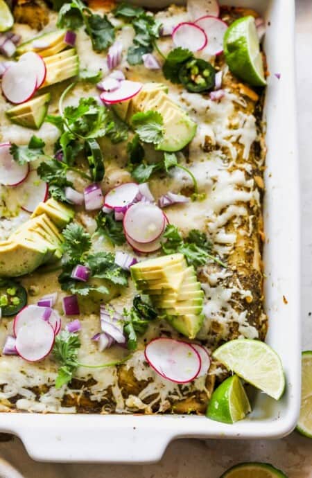 A close up of blackened chicken enchiladas with melty cheese, avocado and cilantro on top