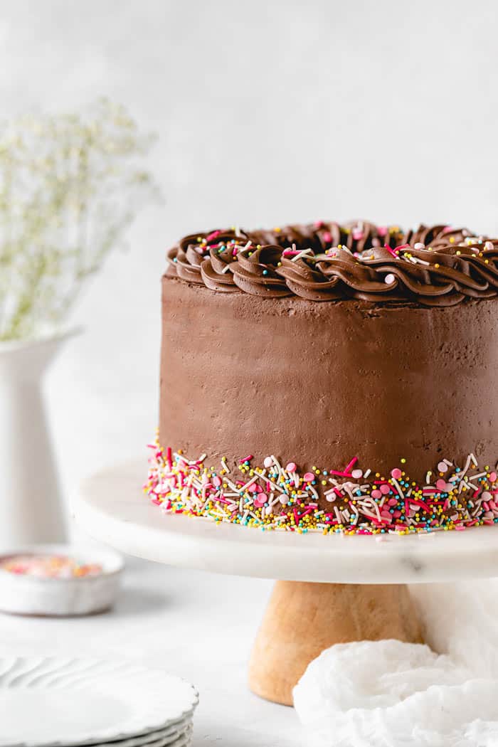 A layer cake with chocolate frosting on it on a white cake stand