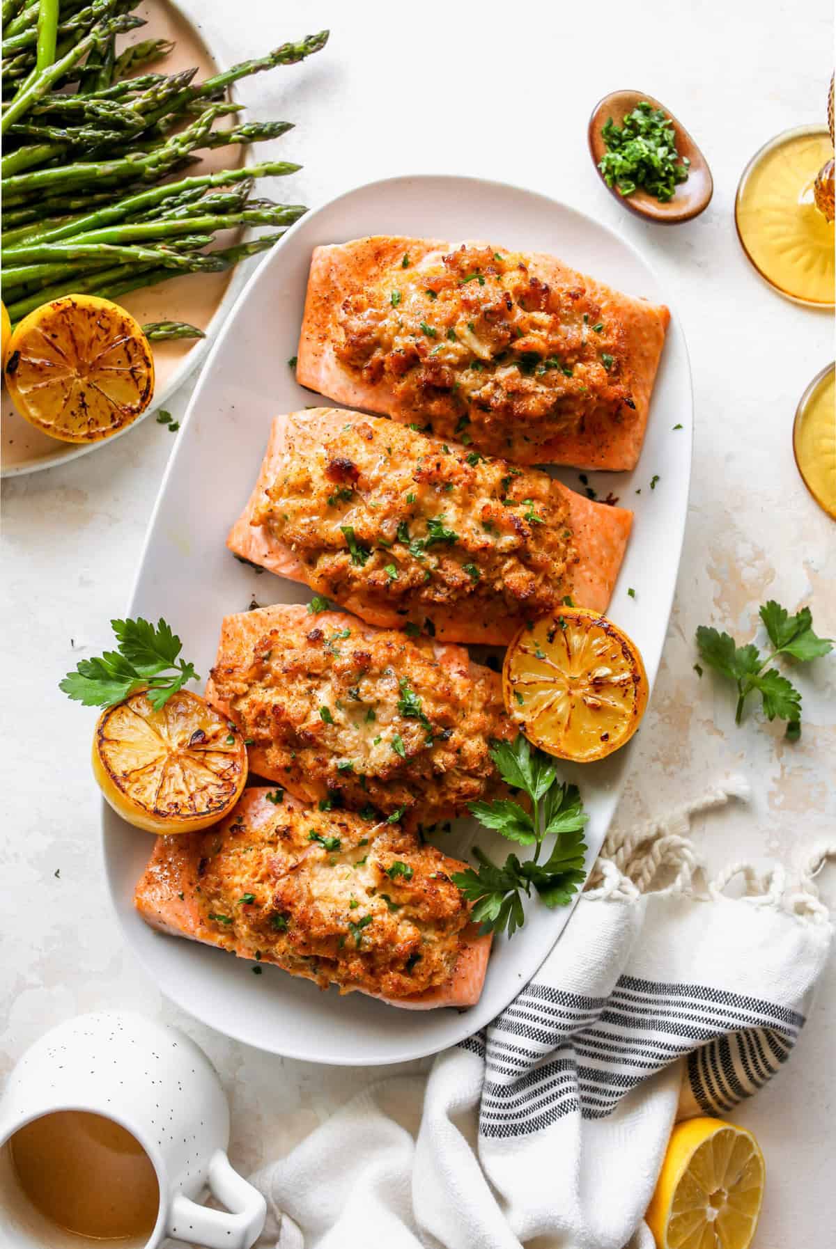 A white platter with four fillets of crab stuffed fish with asparagus and lemon wedges