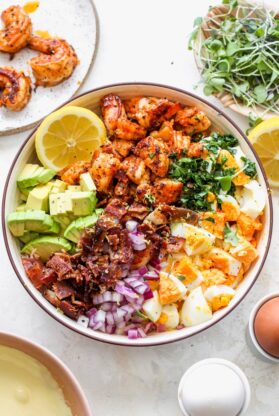 A large bowl filled with avocado, lemon, shrimp, bacon, red onions and boiled eggs