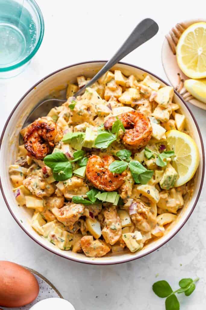 A shrimp egg salad with cajun shrimp on top and a lemon slice