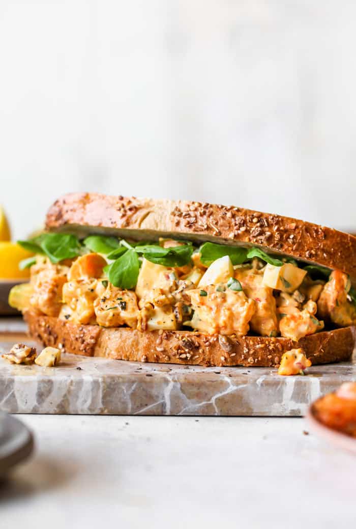 A large egg salad sandwich with parsley on top and microgreens