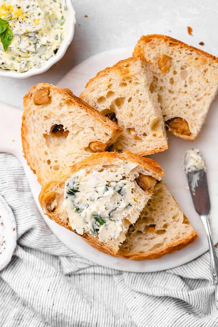 Slices of fresh bread against white background with basil butter smeared on a slice