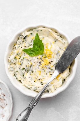 A small white ramekin filled with basil butter and topped with fresh basil and lemon zest