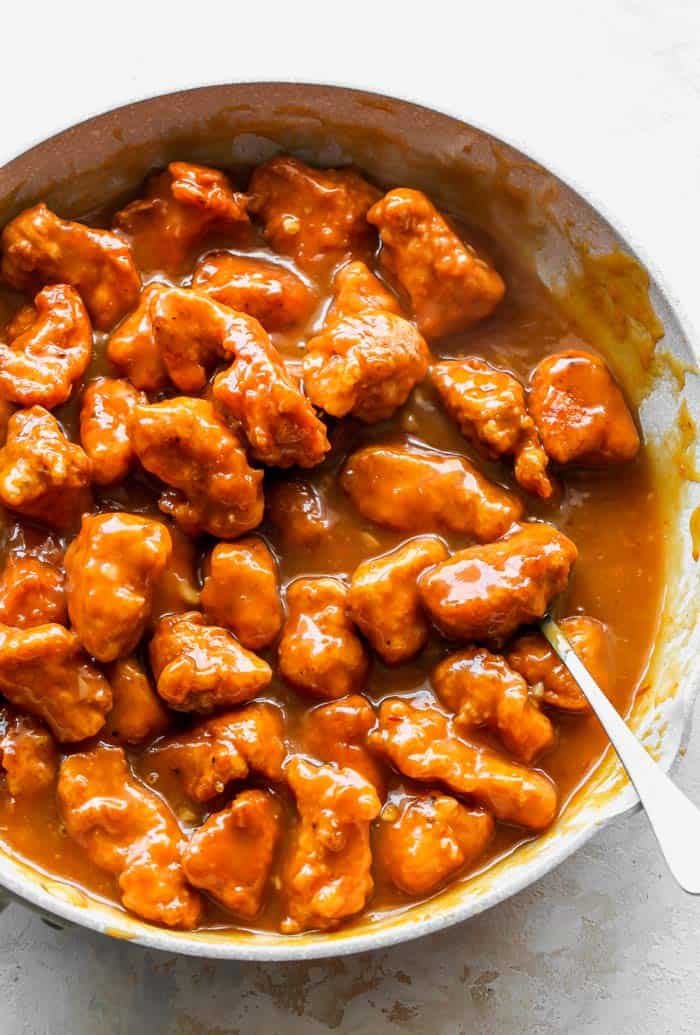 A large skillet of orange chicken pieces coated in a thick glaze