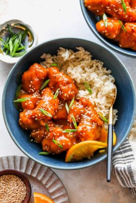 Crispy orange chicken in a blue bowl with sesame seeds over white rice