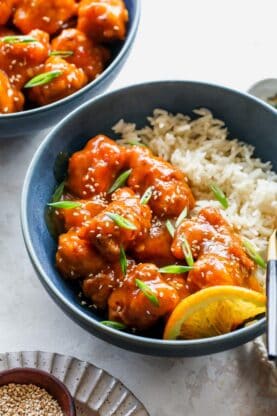 Crispy orange chicken in a blue bowl with sesame seeds over white rice