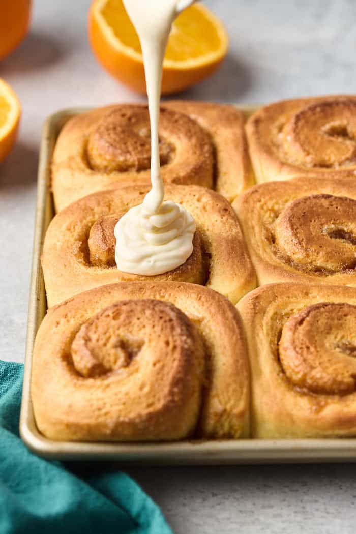 Baked orange cinnamon rolls with an orange glaze being poured over the top