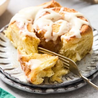 A large orange cinnamon roll on a white plate with fork on the inside prepared to eat
