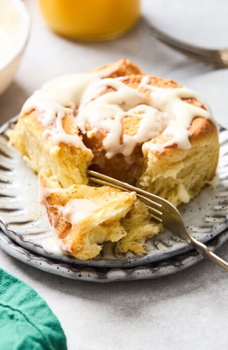 A large orange cinnamon roll on a white plate with fork on the inside prepared to eat