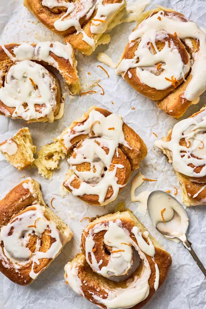 Mimosa orange cinnamon rolls scattered on parchment paper with glaze and zest sprinkled on top