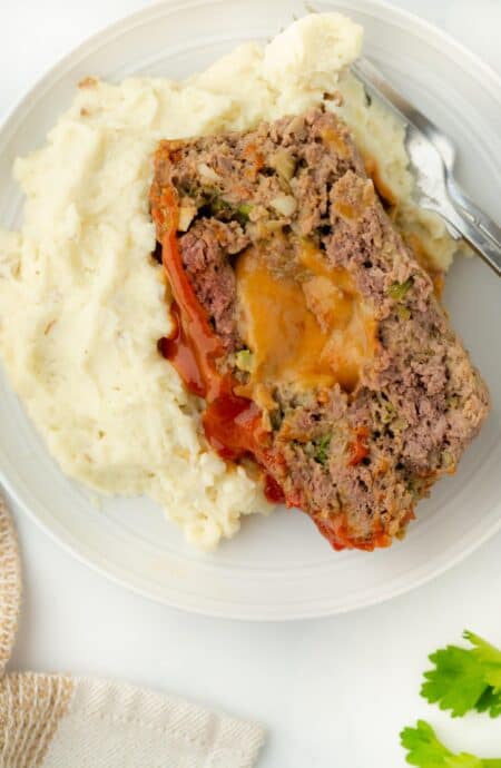 Overhead view of stuffed meatloaf served with mashed potatoes on a plate