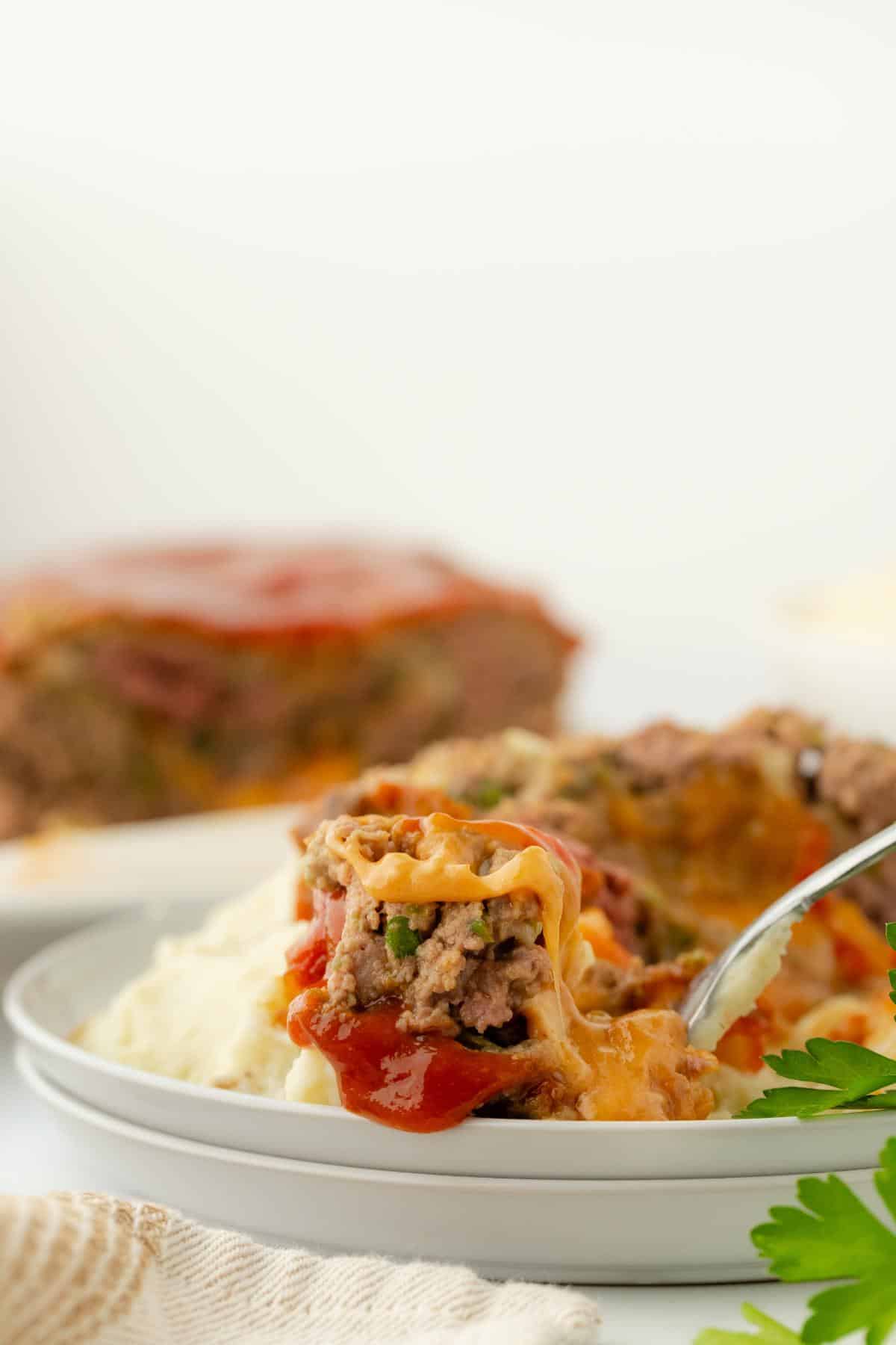 Fork lifting a cheesy bite of stuffed meatloaf from the plate