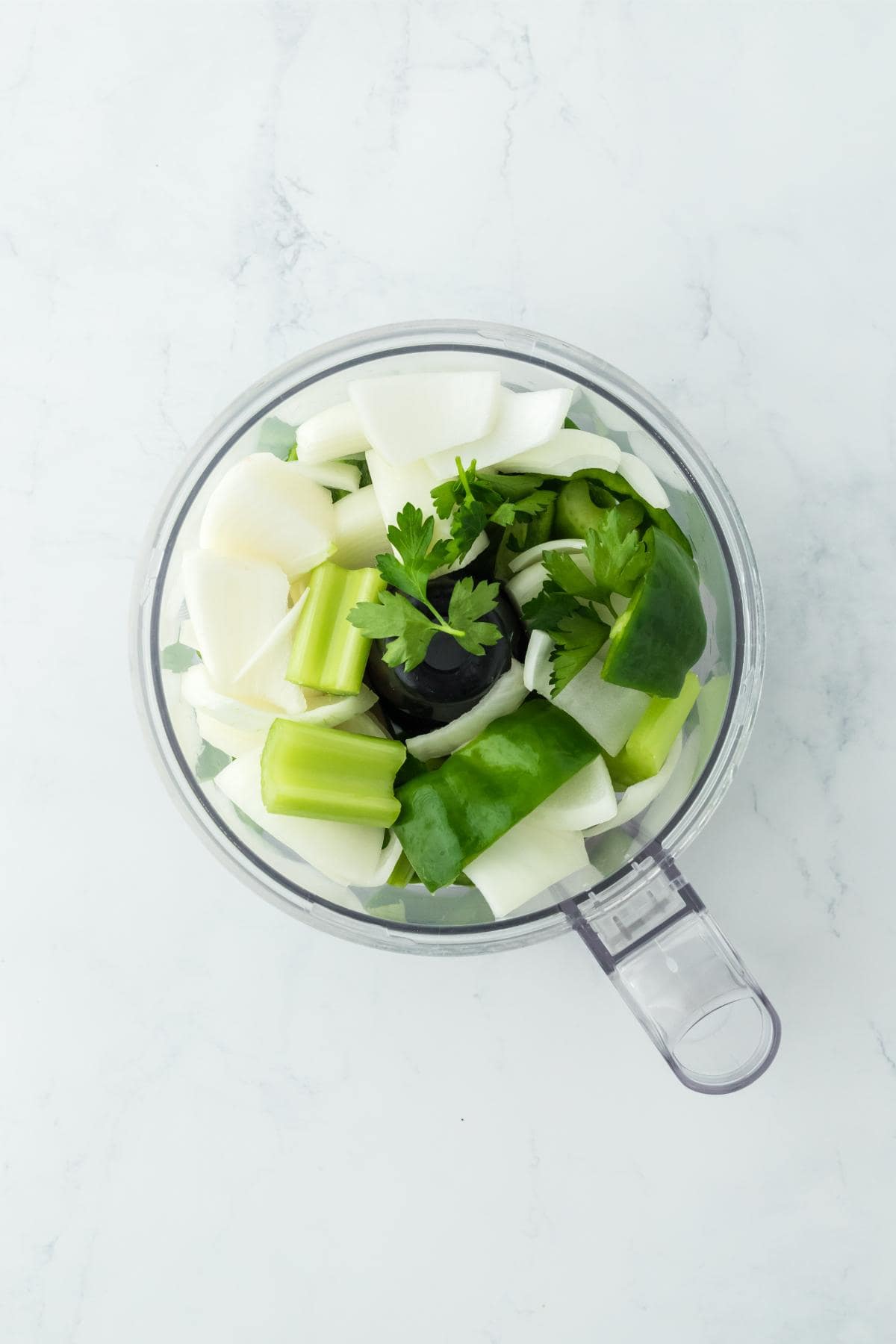 Overhead shot of celery, onion, parsley, and green bell pepper in a food processor bowl