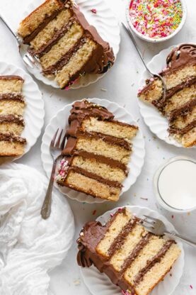 Slices of yellow birthday cake on white plates with chocolate frosting ready to serve