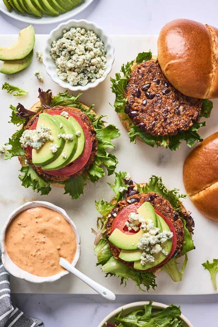 Black bean burgers being assembled with goat cheese, avocado and tomato
