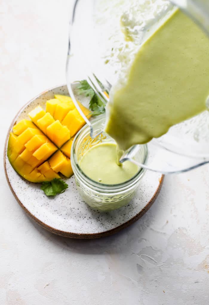 Mango ginger salad dressing being poured into a canister next to sliced mango