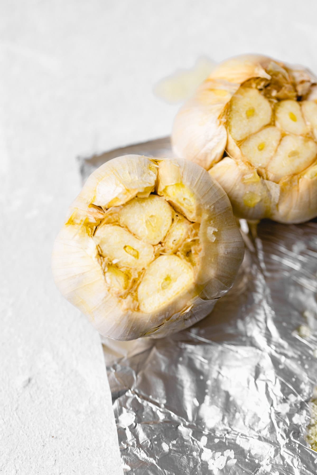 Two heads of roasted garlic on a sheet of aluminum foil, the cloves exposed and lightly browned