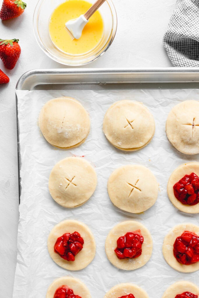 Pie round is crimped on top of strawberry filling for strawberry hand pies on baking sheet pan