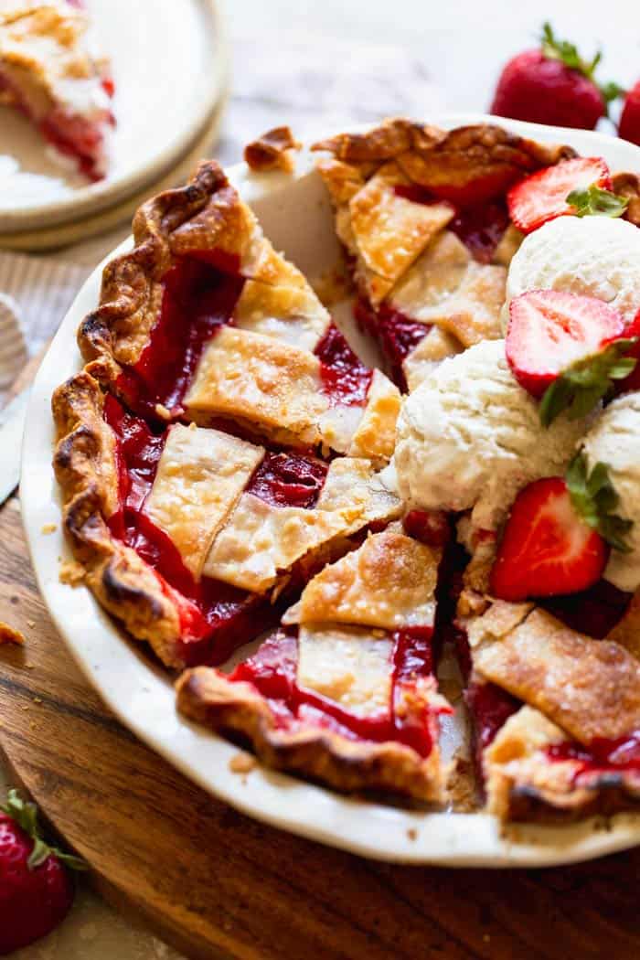 A lattice crust strawberry pie sliced with scoops of vanilla ice cream and slices of fresh strawberries ready to serve