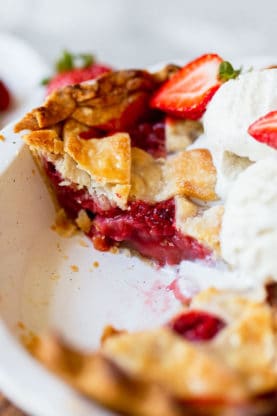 A strawberry pie with slices missing and ice cream melting over