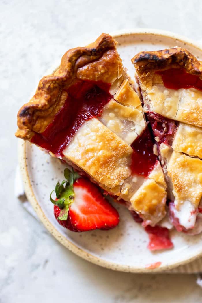 A close up overhead of two slices of double crusted strawberry pie with a slice of strawberry