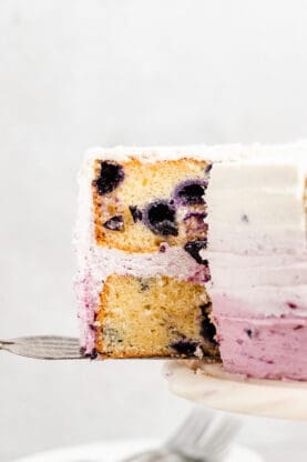 A slice of lemon blueberry cake being removed from layer cake to serve