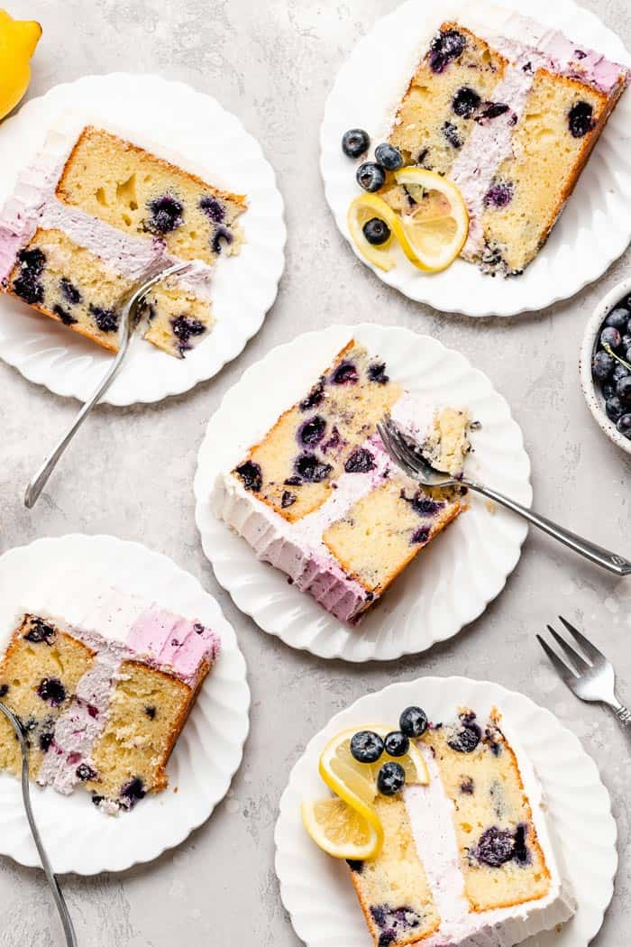 Blueberry lemon layer cake slices on white plates ready to serve with silver forks