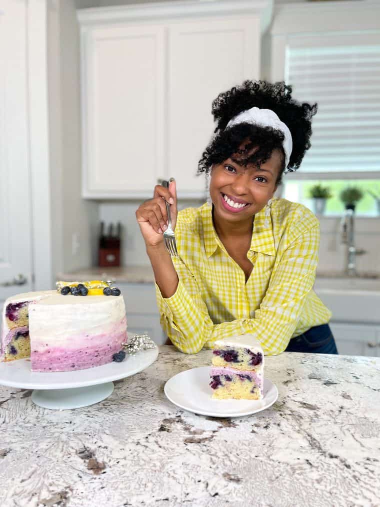 Jocelyn Delk Adams eating a slice of blueberry lemon cake after baking in a yellow gingham shirt