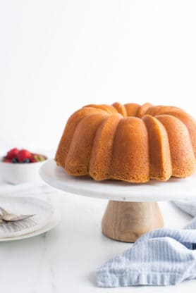 A bundt cake on a white cake stand after being baked