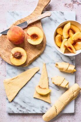 Slices of fresh peaches being wrapped with croissant dough