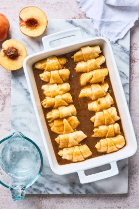 Easy peach dumplings lined up in a baking dish with butter sauce poured on before baking
