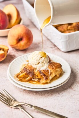 Two pastry baked peach slices on a white plate with vanilla ice cream and butter sauce being poured on top