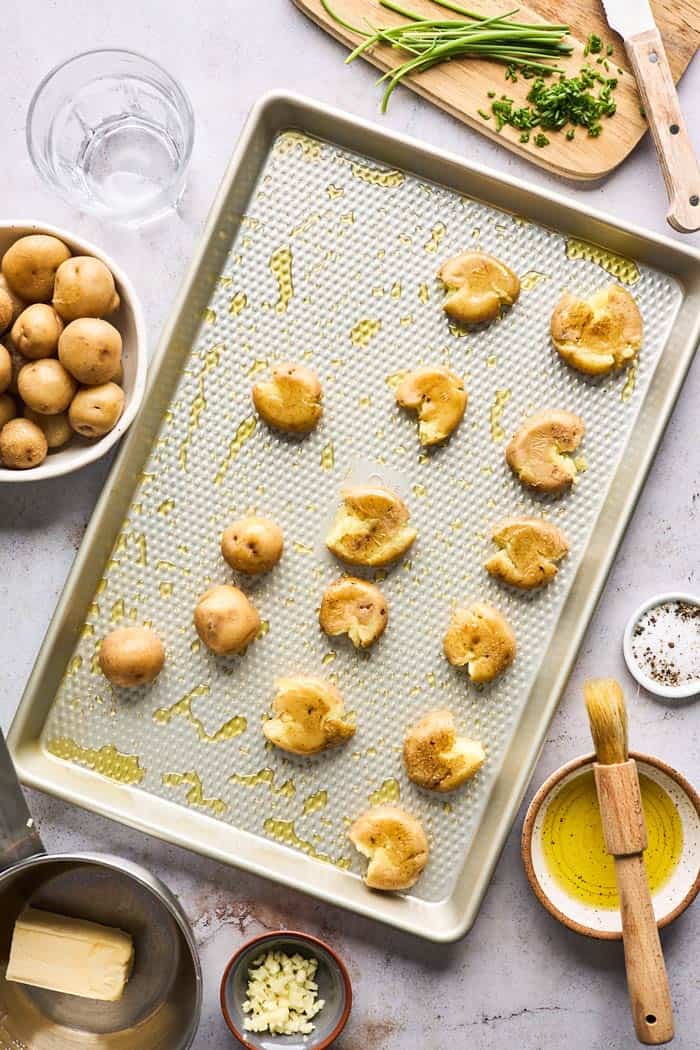 Potatoes on a baking sheet after being mashed and brushed with butter before baking