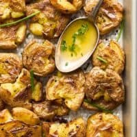 A baking sheet filled with smashed potatoes with garlic butter in a spoon