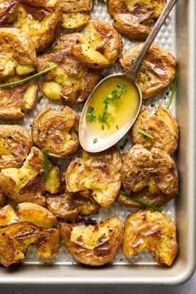 A baking sheet filled with smashed potatoes with garlic butter in a spoon