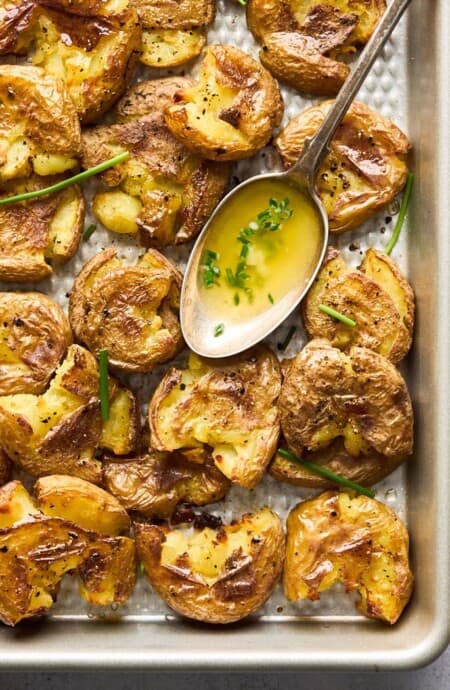 A baking sheet filled with smashed potatoes with garlic butter in a spoon