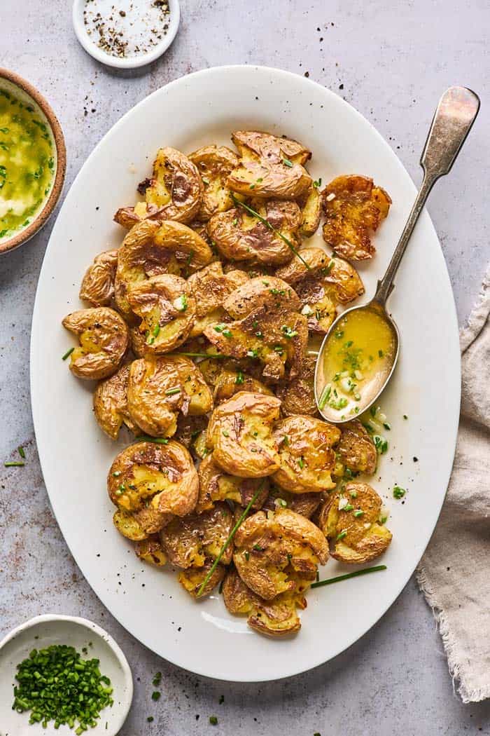 A white platter filled with smash potatoes that have been smashed and drizzled with garlic butter