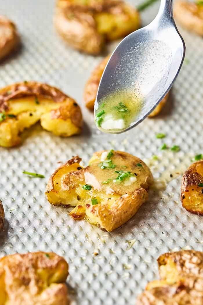 Garlic butter being drizzled over the top of smashed potatoes recipe to serve