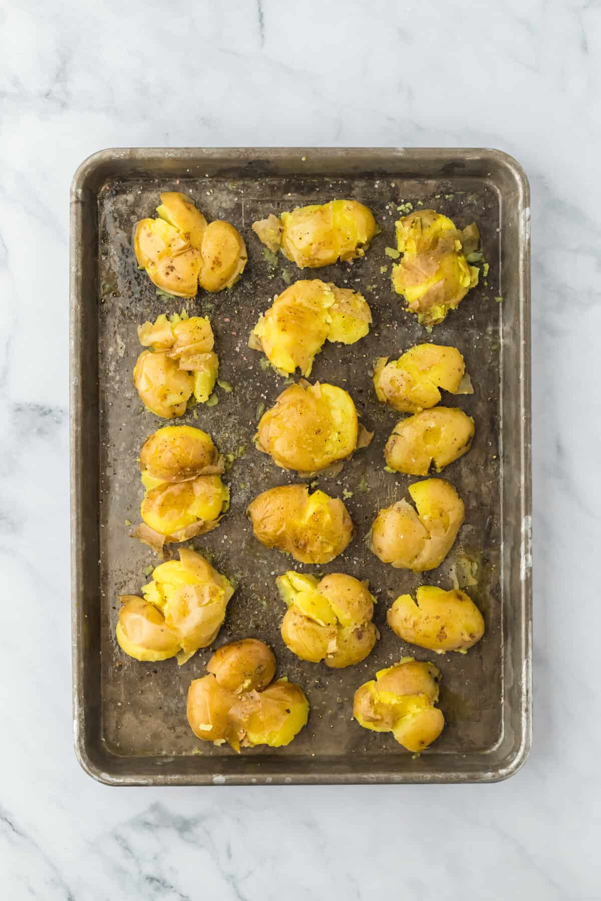 Smashed yukon gold potatoes on a baking sheet on a white countertop