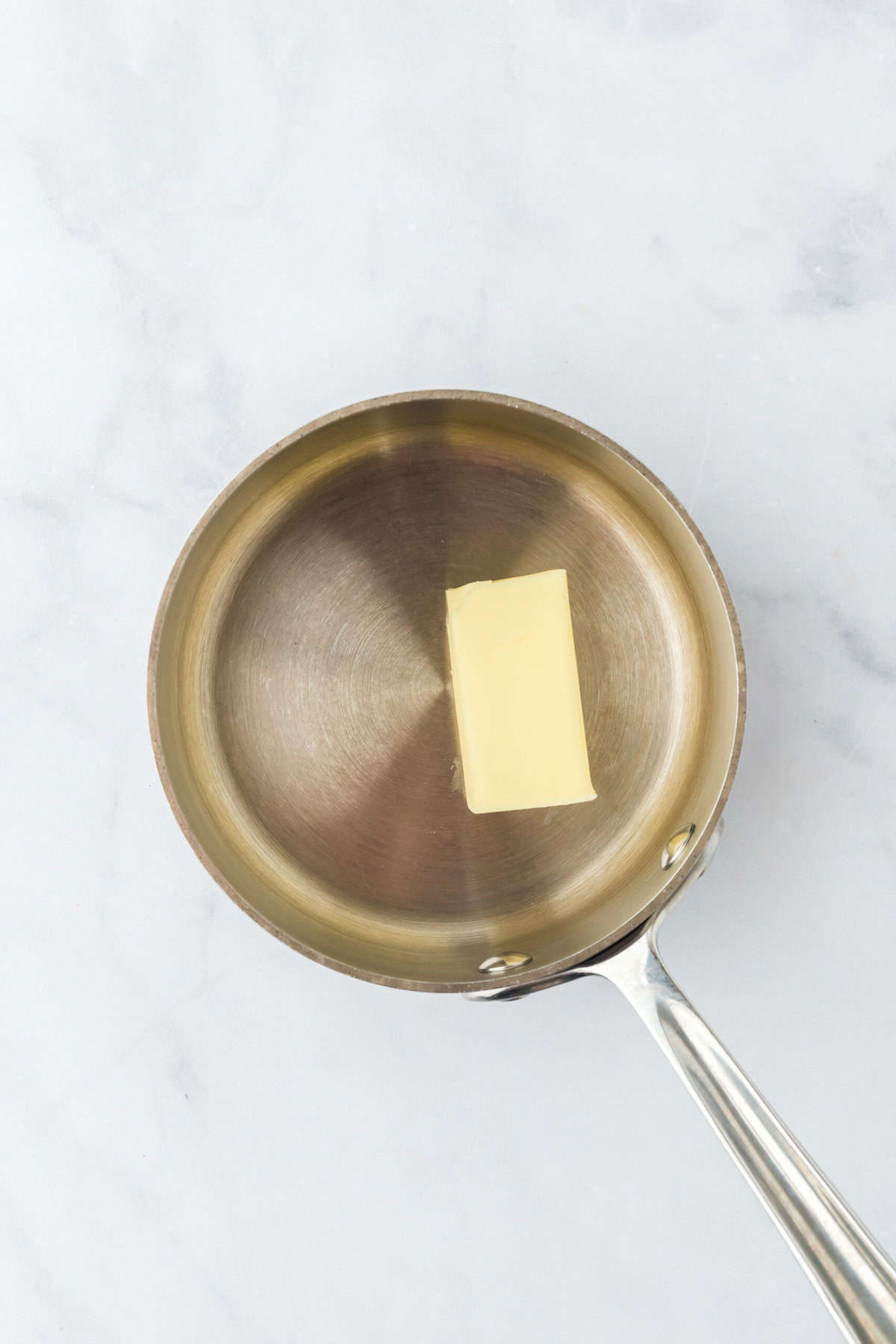 Butter added to a saucepan on a white countertop