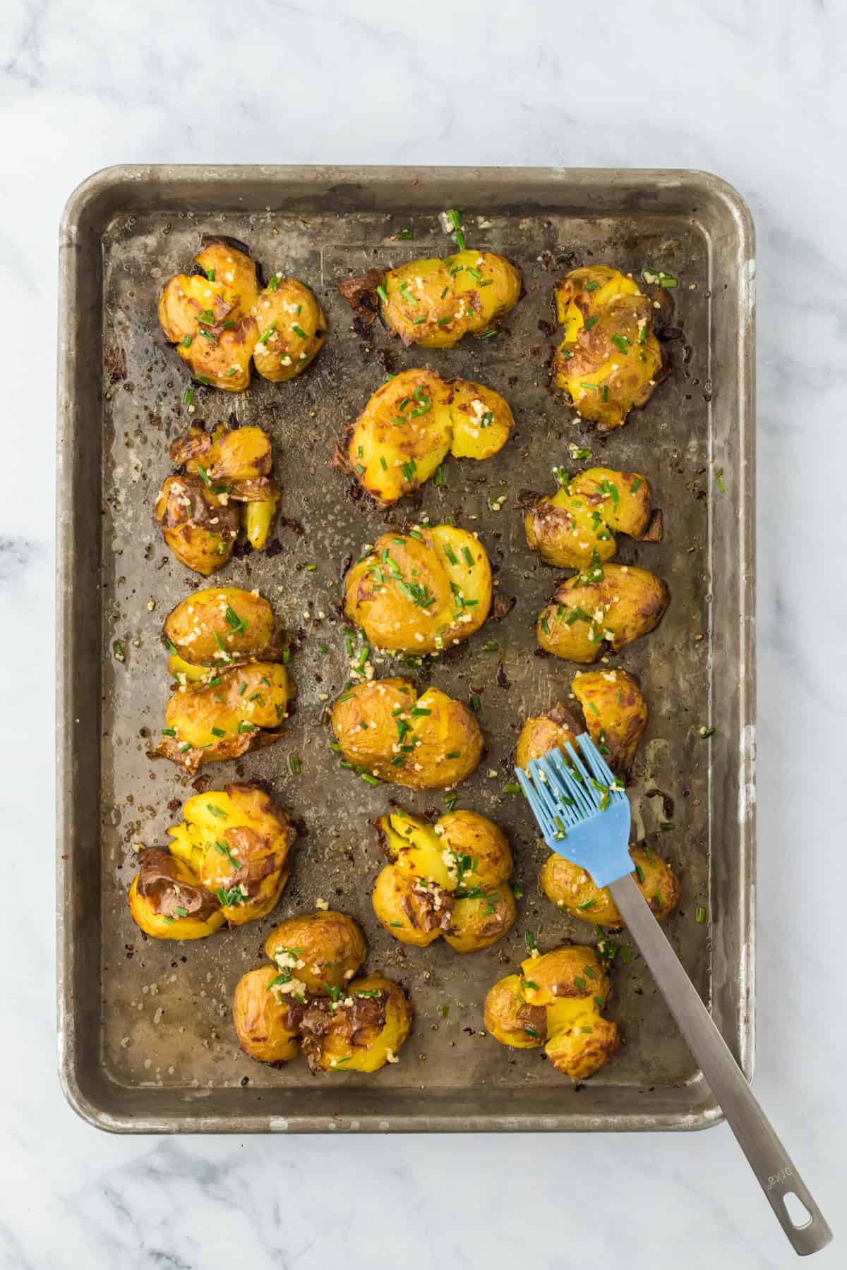 Garlic chive butter brushed on top of smashed yukon gold potatoes on a baking sheet pan