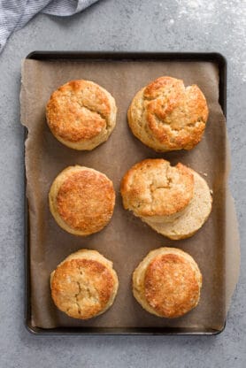 Six tender biscuits made with sour cream on a parchment lined baking sheet after being baked until golden