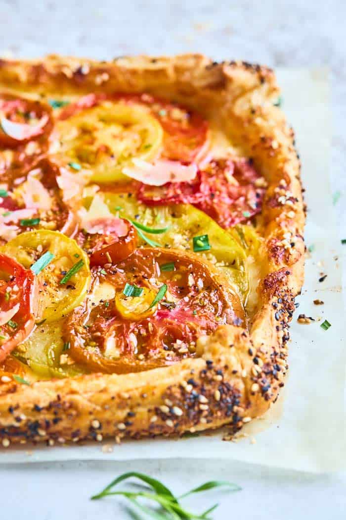 A close up of a freshly baked tomato tart with cheese and tarragon sprinkled on top