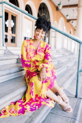Jocelyn Delk Adams sitting on stairs at The Venetian Las Vegas in silk yellow and pink floral dress