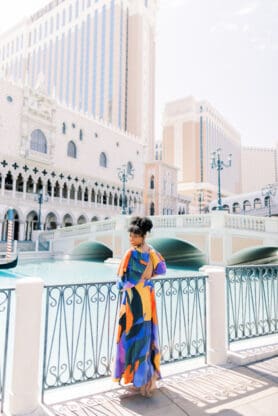 Jocelyn Delk Adams standing next to gondola rides at The Venetian Las Vegas in blue and orange dress
