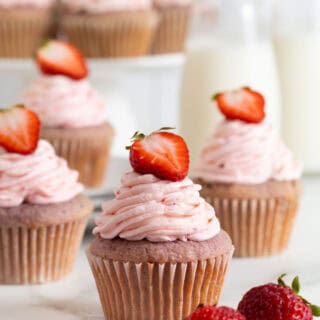 Several strawberry cupcakes on a white countertop with milk in background