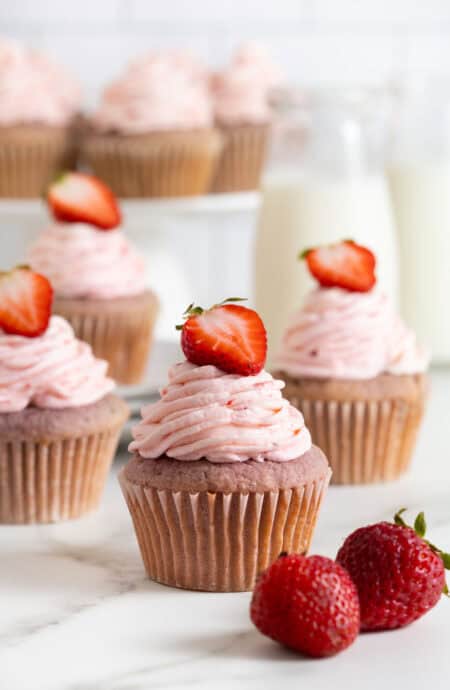 Several strawberry cupcakes on a white countertop with milk in background